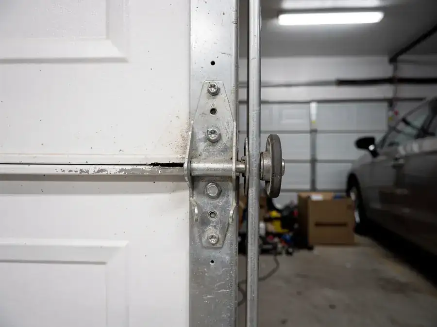 A garage door hinge and roller are attached to a white garage door.