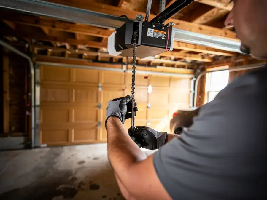 A technician in gloves adjusts the chain on a garage door opener.